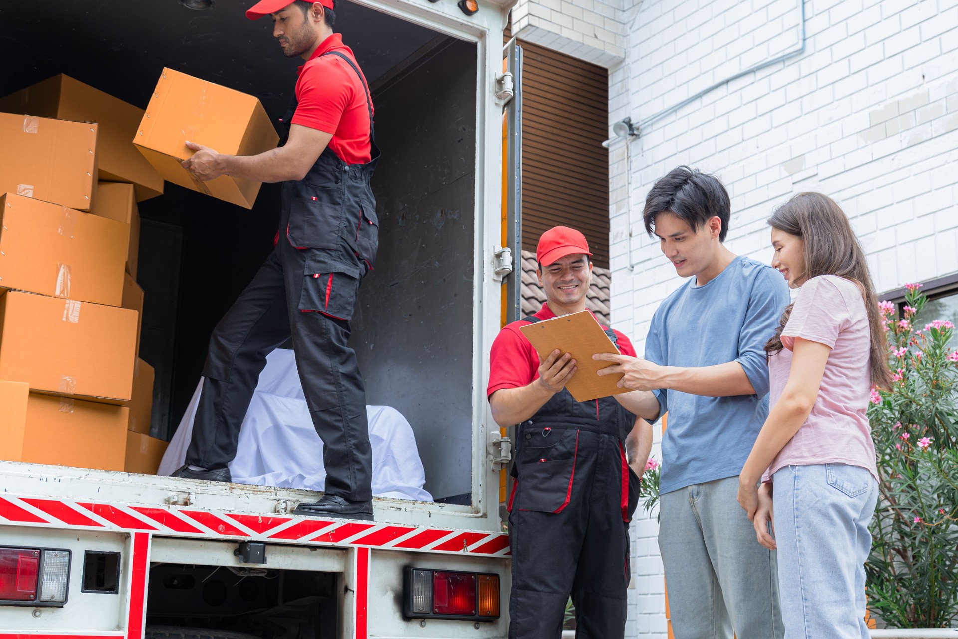Asian couple sign delivery logistic form, checking cardboard box belonging using logistic business service, Multiethnic house moving employees in uniform work professional teamwork in moving company